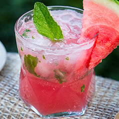 A glass filled with watermelon mojito mocktail. Garnished with mint and watermelon on a table at the coast.