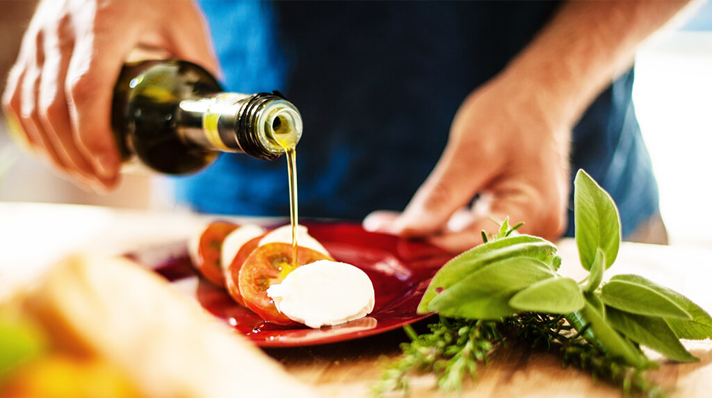 A person drizzling olive oil over tomato and mozzarella slices.