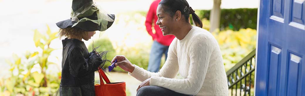 Woman handing out a candy bar to a child who is trick-or-treating