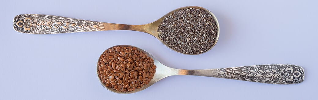 A spoonful of chia seeds next to a spoonful of flax seeds.