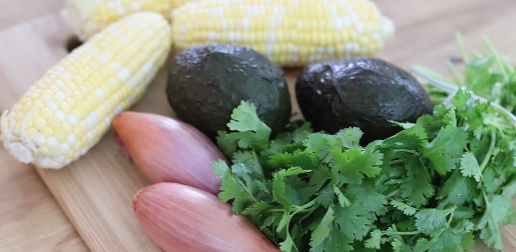 corn, shallots, avocado, and cilantro on a cutting board.