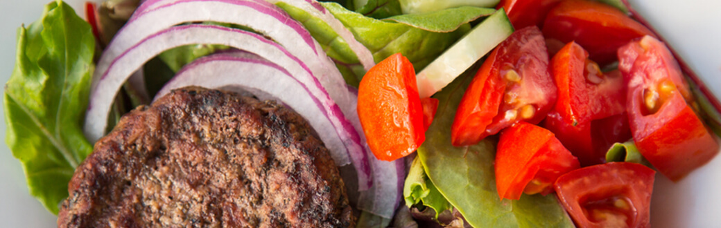 Deconstructed Burger Salad Recipe. A hamburger patty on top of vegetables and drizzled with a creamy chipotle sauce.