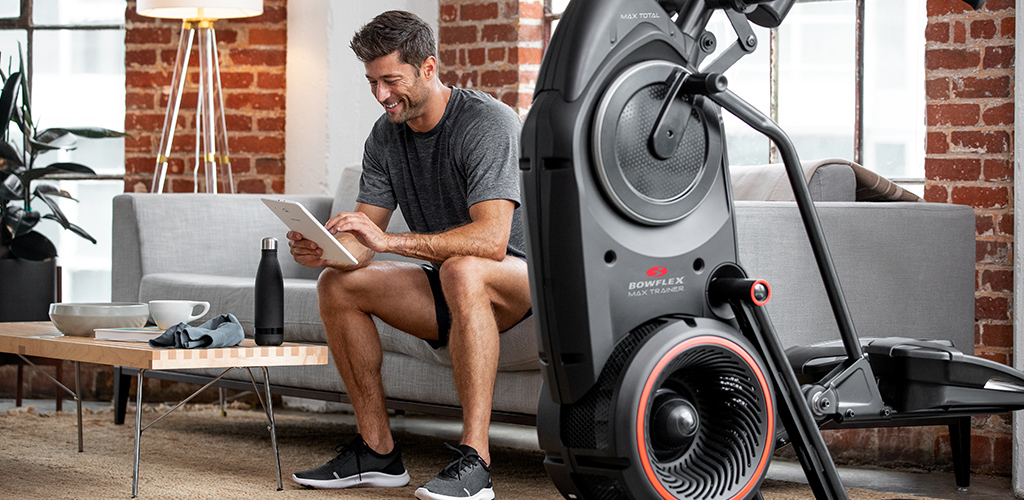 A man sitting next to a BowFlex Max Trainer