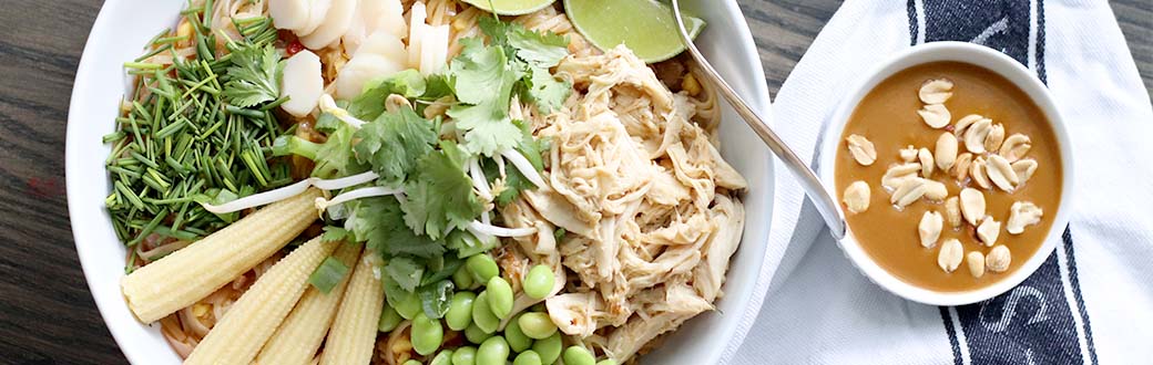 Bowl of Pad Thai noodles topped with shredded chicken, corn, edamame and cilantro.  Peanut sauce served on the side.