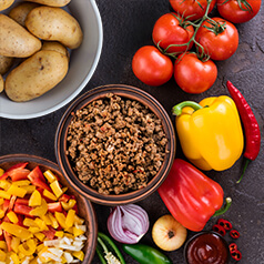 closeup of cooked ground beef in a bowl surrounded by bell peppers and other vegetables.