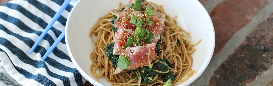 Seared tuna with spinach and whole wheat noodles in a white bowl.