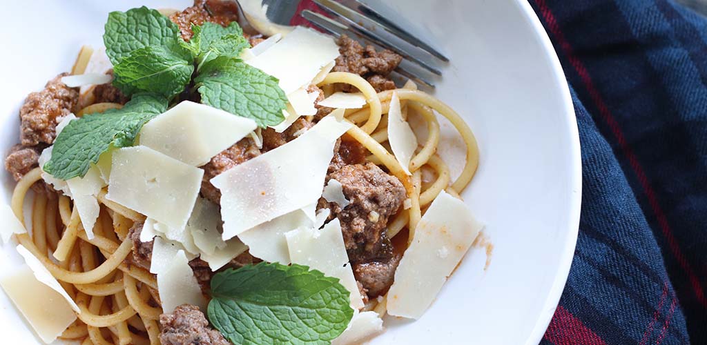 Close up of lamb Bolognese served on bucatini pasta.