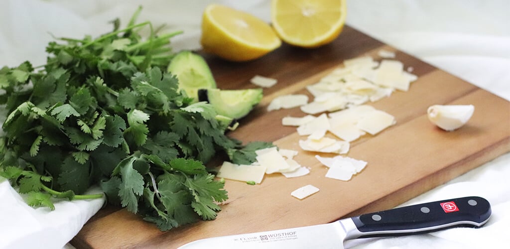 Cilantro, sliced avocado, lemon, and shaved parmesean cheese on a wood cutting board.