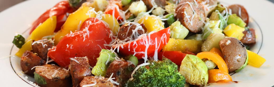 Roasted vegetables with sausage and Parmesan cheese on a plate.