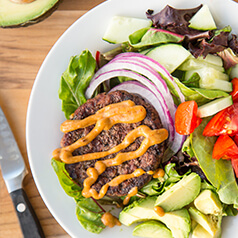 Close up image of burger salad. Hamburger patty on top of vegetables.