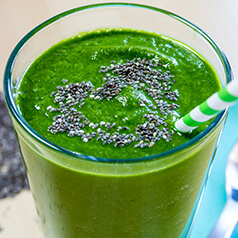 close up image of a peachy green smoothie in a glass with a straw.