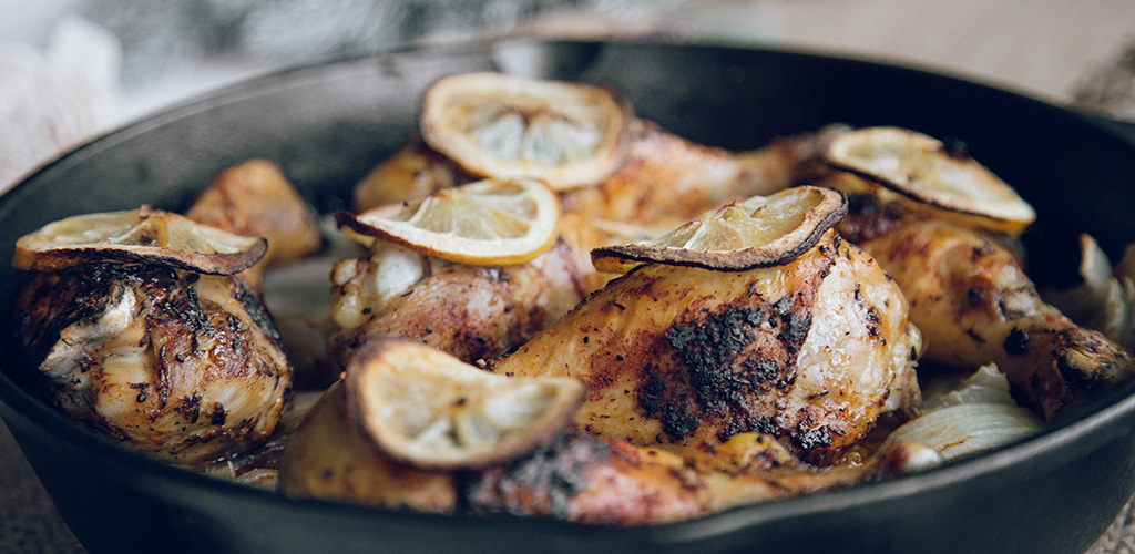 Roasted chicken legs topped with lemon slices in a cast iron skillet