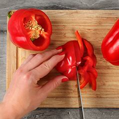 A person chopping a red bell pepper.