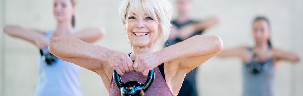 mature woman doing a kettlebell workout in a group class