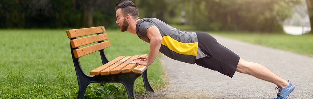Man performing an elevated pushup using a park bench